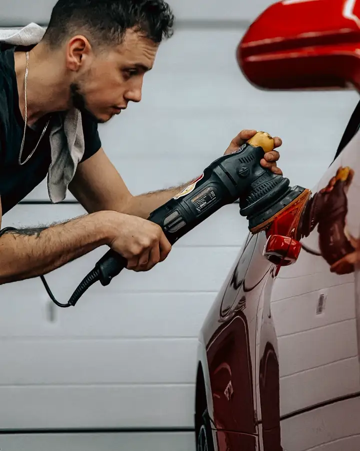 A detailer machine polishing a red car