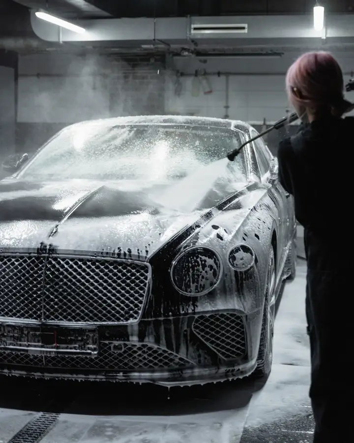 A dark luxury car covered in foam during a hand wash